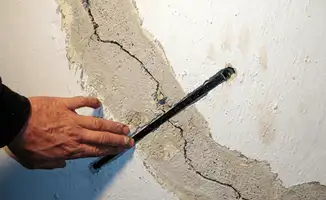 A wall with a large crack is being inspected by a professional in Overland Park, KS